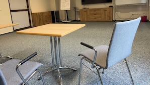Une salle de conférence équipée d’une table, de deux chaises, d’un tableau blanc, d’un téléviseur et d’une poubelle rouge.