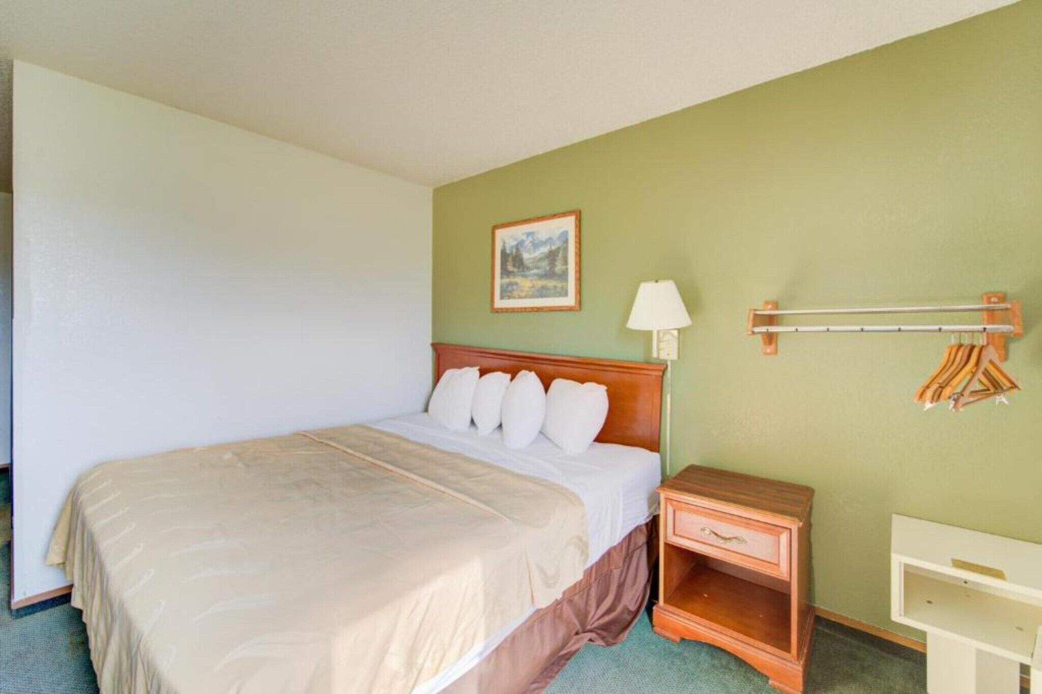 A hotel room with a bed, bedside table, lamp, and a coat rack.