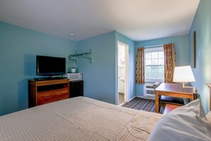 Una habitació d'hotel amb un llit, una televisió, una taula i una finestra amb cortines.