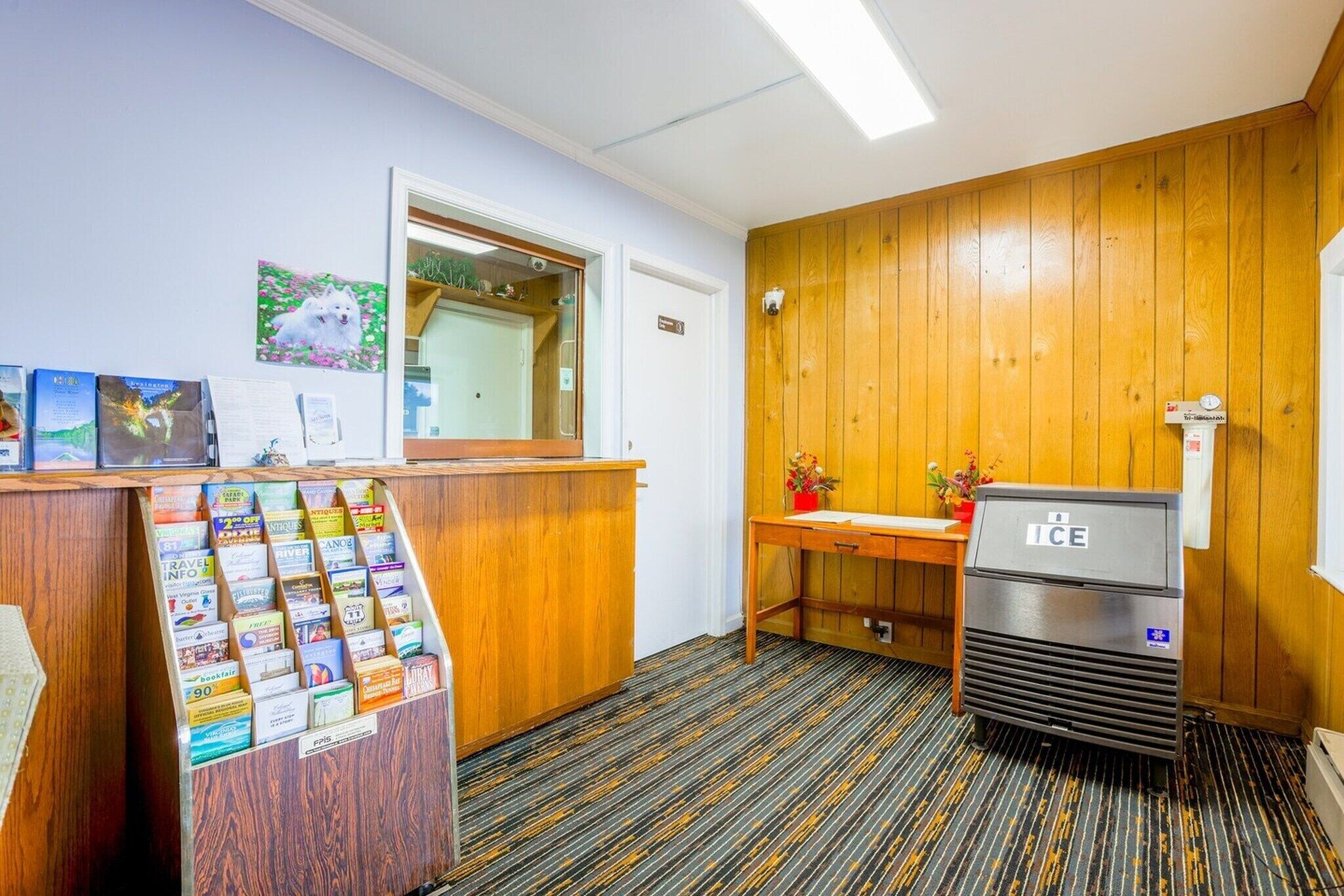 A reception area with a wooden desk, a refrigerator, a mirror, and a wall-mounted information board.