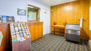 En reception med et træbord, et køleskab, et spejl og en opslagstavle på væggen.