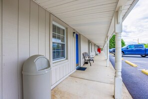 A motel with a covered walkway, a trash can, a bench, and a blue car parked outside.
