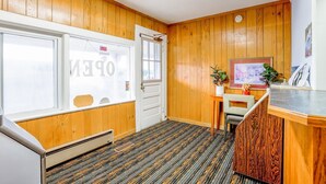 Un vestíbulo de hotel con paneles de madera, un mostrador de recepción, un cuadro enmarcado en la pared y una puerta con ventana.
