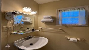 A bathroom with a sink, mirror, hairdryer, towel rack, and window with curtains.