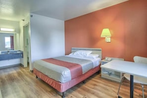 Una camera d'albergo con un letto, un comodino, una lampada e vista sul bagno.