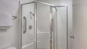 A glass-enclosed shower stall with a white wall, a towel rack, and a door with a handle. - Queen Bed with Refrigerator (New Cumberland, PA)