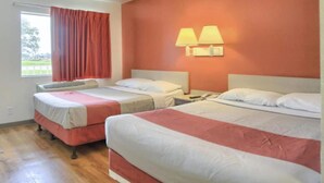 Hotellihuone, jossa on kaksi sänkyä, ikkuna, jossa on verhot, ja seinään kiinnitetty valaisin.