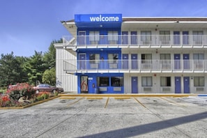 Un motel de varios pisos con un cartel de 'welcome', un estacionamiento y un coche estacionado al frente.
