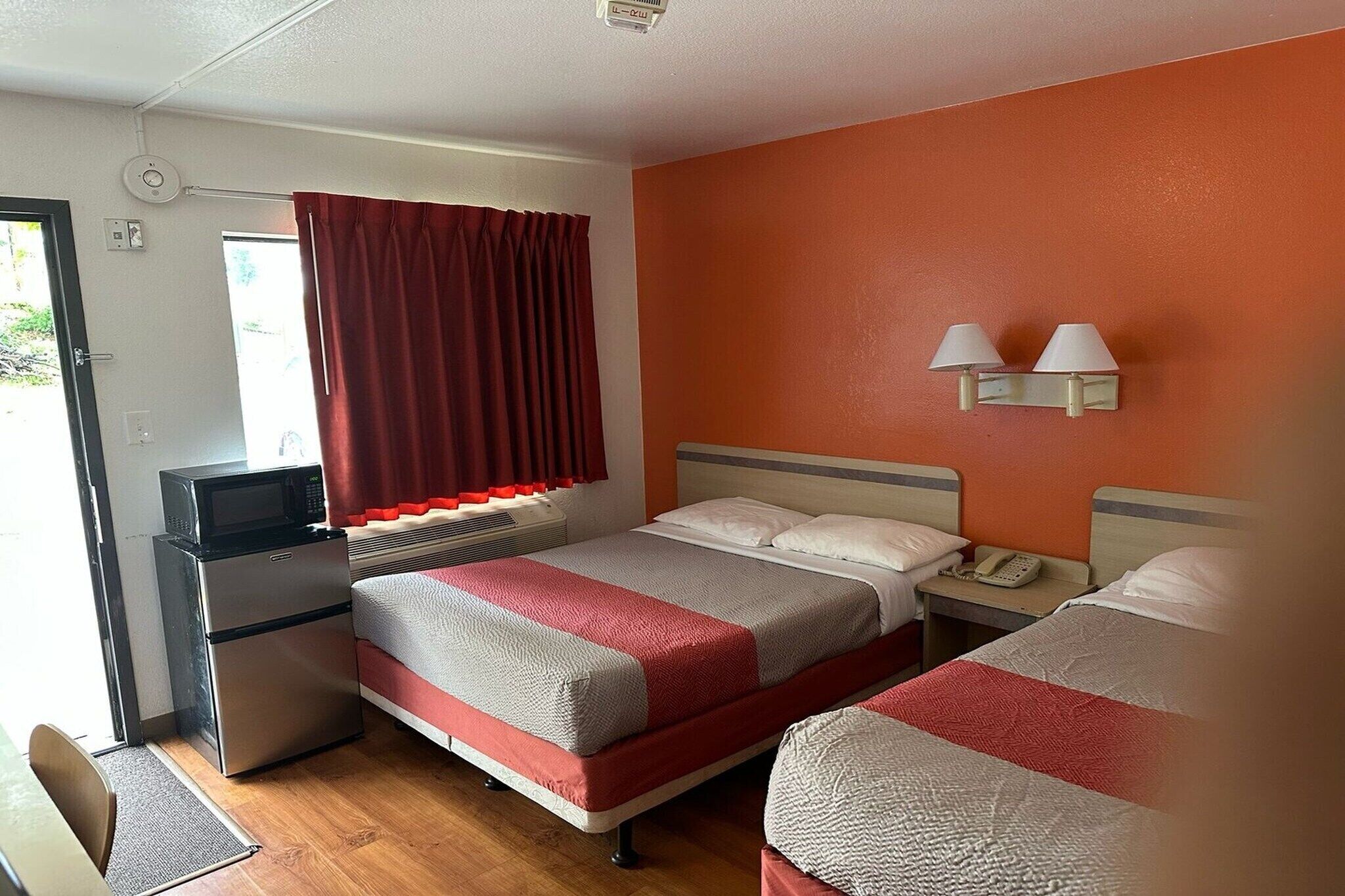 Une chambre d’hôtel avec deux lits, un four à micro-ondes, un petit réfrigérateur, un bureau avec un téléphone et une fenêtre avec des rideaux.