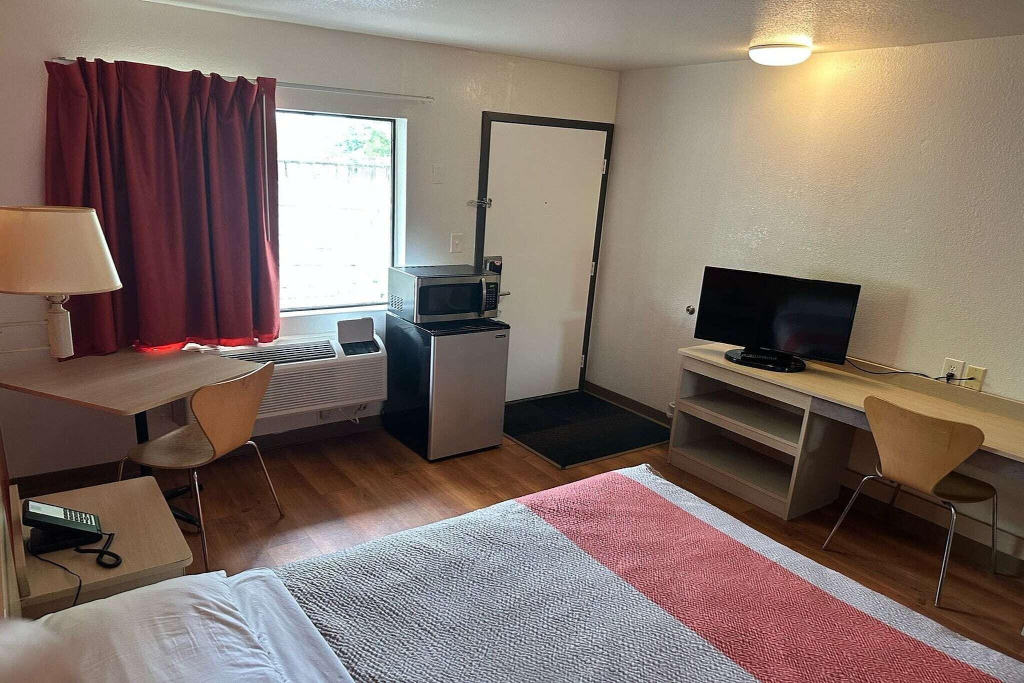 Une chambre d’hôtel équipée d’un lit, d’un bureau, d’une chaise, d’une télévision, d’un four à micro-ondes et d’un petit réfrigérateur.