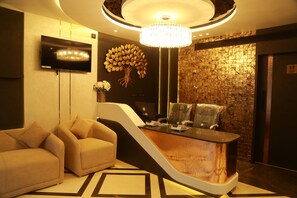 A reception area with a curved reception desk, a flat-screen TV, a chandelier, and a wall with a textured pattern.