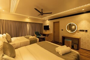 A hotel room with two beds, a ceiling fan, a TV, a fireplace, and a round mirror.