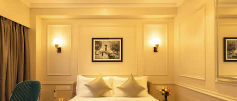 A hotel room with a bed, two wall-mounted lamps, a framed picture, a chair, a nightstand, and a vase with flowers.