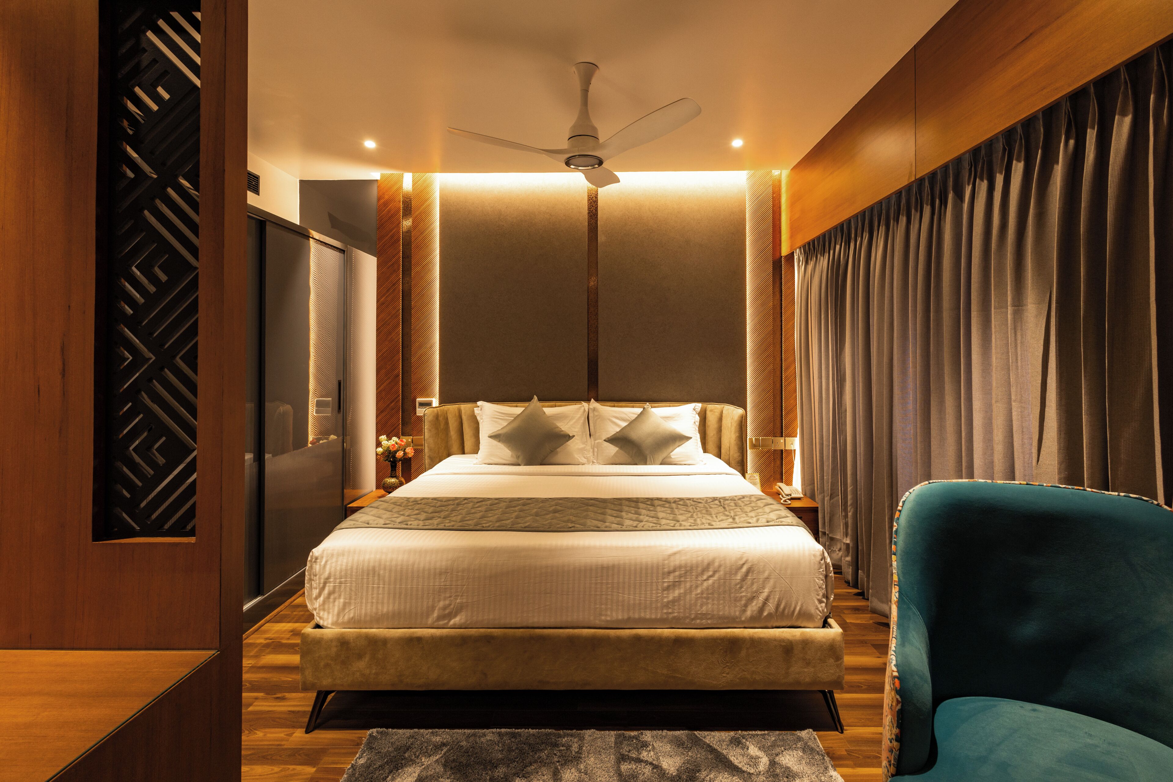 A modern bedroom with a large bed, a ceiling fan, and a blue armchair.