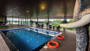 Piscina interior con vista al exterior, rodeada de sillones de descanso y plantas en macetas.