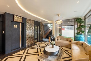 A modern lobby with a geometric floor pattern, a reception desk, a chandelier, and a staircase leading to upper floors. - Paramount Residency (Nedumbassery)
