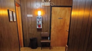 A carpeted hallway with wooden walls, a trash bin, a chair, and a door with a sign.