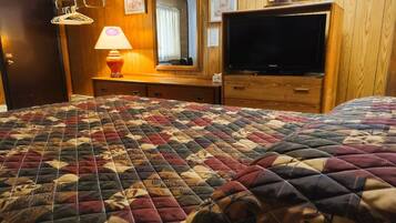 Hotellihuone, jossa on suuri sänky, televisio, puinen lipasto, peili ja lamppu.