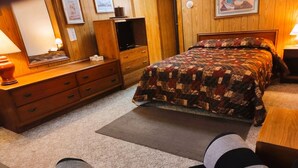 A bedroom with a bed, dresser, mirror, and a television.