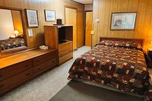 A bedroom with a wooden wardrobe, a bed with a quilt, a dresser, and a mirror.