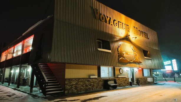 A hotel with a sign reading 'VOYAGEUR HOTEL' and a large, illuminated fish sculpture on the facade.