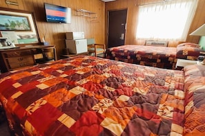 A hotel room with two beds, a television, a desk with a computer, and a door.