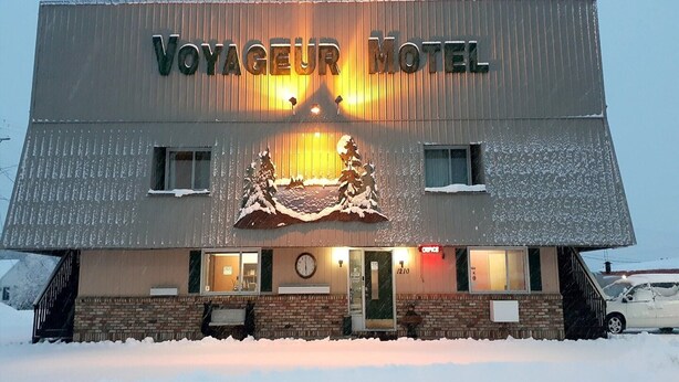 En bygning med et skilt, der viser 'Voyageur Motel', og et tag dækket af sne.
