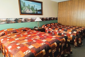 A hotel room with two beds, a painting of a forest scene, a wooden headboard, and a lamp on the nightstand. - International Falls | 2 full bed (International Falls)
