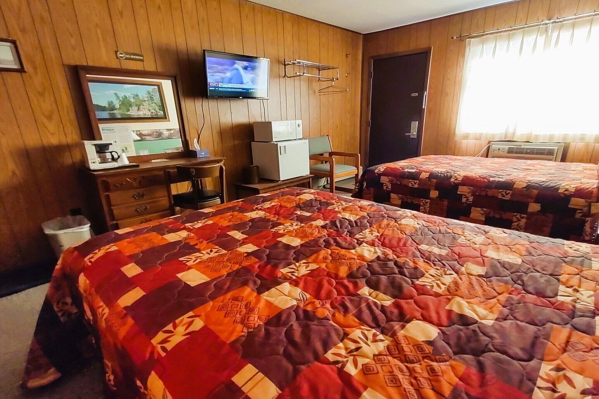 A hotel room with two beds, a desk with a computer, a television, and a window with curtains.