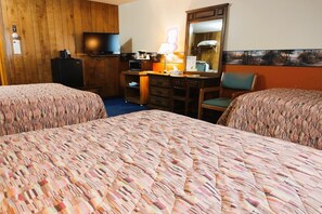 A hotel room with two beds, a desk with a lamp, a television, and a painting on the wall. - 2 Full Beds with 1 Twin Bed & Rollaway (International Falls)