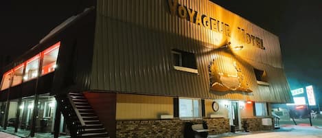 Un hotel con un letrero que dice 'VOYAGEUR HOTEL' y una gran escultura de pez iluminada en la fachada.