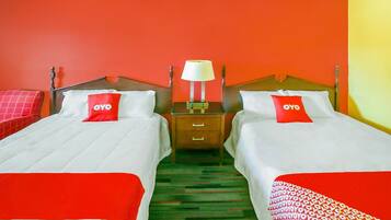 A hotel room with two beds, each with a red pillow and a white bedspread. There is a nightstand with a lamp between the beds.