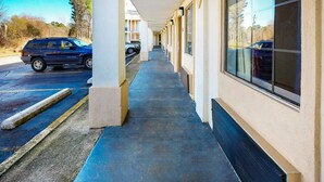 Un couloir d’hôtel avec une galerie couverte, un VUS garé et un bâtiment doté de grandes fenêtres.