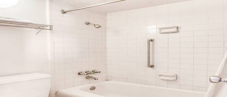 A bathroom with a white bathtub, toilet, and shower area.