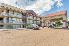 A multi-story hotel with a lobby area, a parking lot, and a car parked in front.