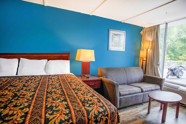 A hotel room with a large bed, a sofa, a small table, and a window with curtains.