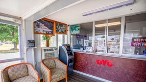 Ein Empfangsbereich mit einer Rezeption, einer digitalen Uhr, einem Automaten und zwei Sitzgelegenheiten mit Muster.