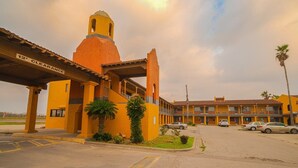A building with a tower, a covered entrance, and a parking lot with cars. - Kingsville | King Bed (Kingsville)