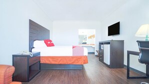 A hotel room with a bed, a desk, a chair, a TV, and a lamp. - Kingsville | King Bed (Kingsville)