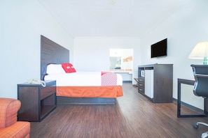 A hotel room with a bed, a desk, a chair, a TV, and a lamp. - Kingsville | King Bed (Kingsville)