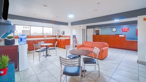 Un hall de hotel con una recepción, una zona de cocina y un área de descanso con mesas y sillas.