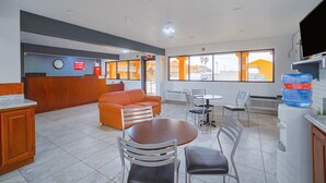 Un hall de hotel con mostrador de recepción, un sofá, mesas de comedor, sillas y un dispensador de agua grande.