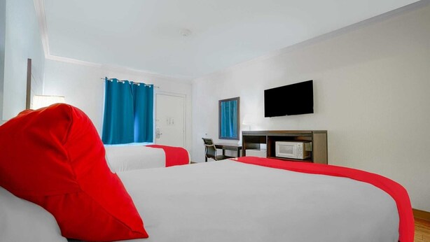 Habitación de hotel con dos camas, un escritorio, televisión y ventana con cortinas.