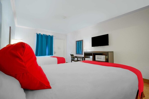 Habitación de hotel con dos camas, un escritorio, televisión y ventana con cortinas.
