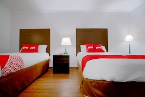 Ein Hotelzimmer mit zwei Betten, jeweils mit Kopfteil, Nachttisch und Lampe.