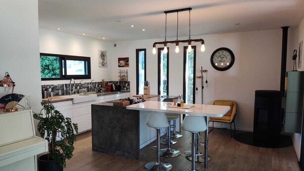 Una cocina moderna con una isla central, taburetes de bar, un televisor y un reloj en la pared.