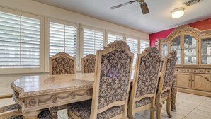 Un comedor con una mesa de mármol y sillas con estampado floral, un ventilador de techo y un armario con puertas de cristal.