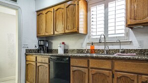 Una cocina con armarios de madera, lavavajillas, cafetera y ventana con persianas.