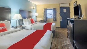 A hotel room with two beds, a desk, a TV, and a window with curtains.