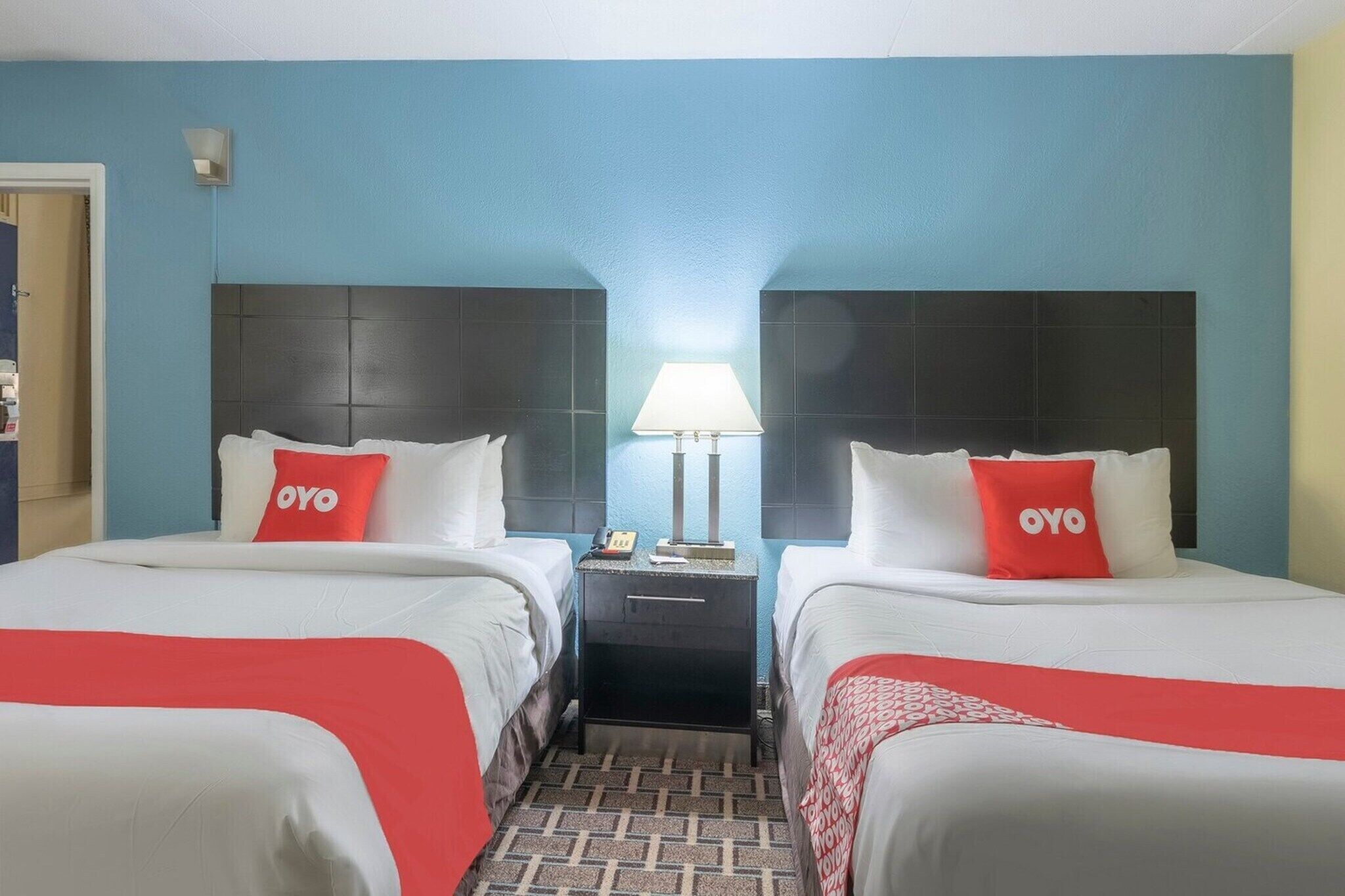 Una habitación de hotel con dos camas, una mesita de noche, una lámpara y una puerta.